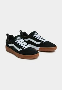 Sneaker in suede nero con design a strisce bianche, lacci bianchi e suola in gomma naturale. Presenta un collo imbottito e un logo sulla linguetta.