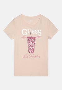 Majica s kratkim rukavima u breskvasto ružičastoj boji s grafikom šolje ukrašenom u ružičastoj boji i slamčicom, te natpisom "GUESS Est. 1981 Los Angeles" u bijeloj i ružičastoj boji.