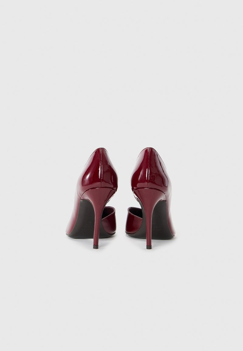 Glänzende burgunderfarbene Lackleder-Pumps mit spitzen Zehen und schmalen Stiletto-Absätzen, die eine glatte Textur und ein elegantes Design zeigen.
