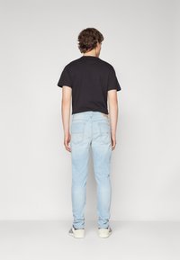 Camiseta negra de manga corta para hombre combinada con jeans slim-fit de color azul claro. Los jeans tienen bolsillos traseros y detalles de costura sutiles.