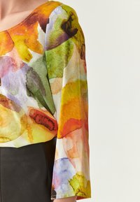 Blouse multicolore avec un motif floral en aquarelle ; fabriquée en tissu léger ; dotée d'un large col et de manches longues et amples.