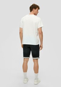 T-shirt en coton blanc, short en jean noir avec revers, baskets blanches et chaussettes grises. Pas de motifs visibles, design épuré.