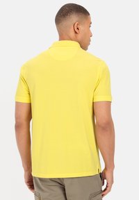 Gelbes Poloshirt aus Baumwolle, mit klassischem Kragen, kurzen Ärmeln und geradem Saum. Glatte Textur, minimale Details.