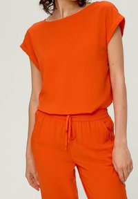 Orange top med korte oprullede ærmer, lavet af glat stof. Sammen med matchende bukser med elastisk talje og snørrebånd.