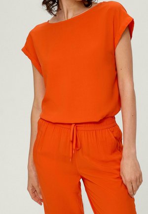 Oranje top met korte omgerolde mouwen, gemaakt van gladde stof. Gecombineerd met bijpassende elastische broek met een trekkoord.