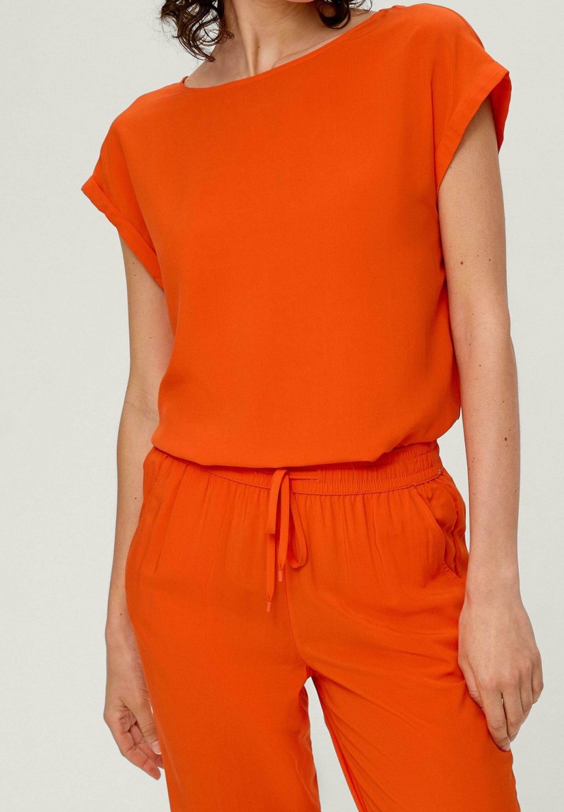 Orange top med korte oprullede ærmer, lavet af glat stof. Sammen med matchende bukser med elastisk talje og snørrebånd.