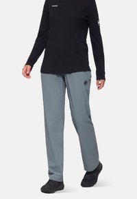 Lichte, grijze outdoorbroeken met een losse pasvorm, voorzien van een zwart logo op het been. Gecombineerd met een zwart shirt met lange mouwen.
