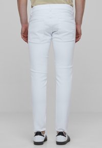 Biele slim-fit džínsy s hladkou textúrou, obsahujúce dve zadné vrecká a pútka na opasok. Skombinované s čierno-bielymi teniskami.