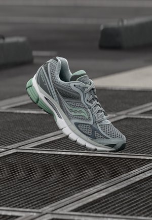 Zapatilla deportiva gris con parte superior de malla, detalles en verde menta y suela acolchada. Presenta secciones reforzadas en la puntera y el talón para mayor soporte.