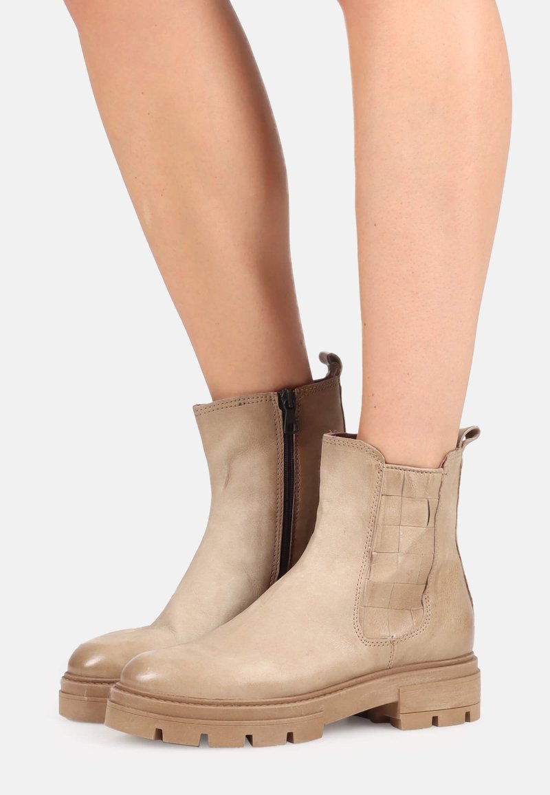 Bottines beiges avec semelles épaisses, zips sur les côtés, détail en cuir tressé sur le côté extérieur, portées sur des jambes nues.
