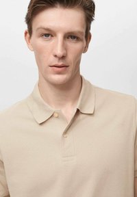 Beige Poloshirt aus strukturiertem Material, mit Kragen und drei Knöpfen am Hals. Einfaches und klassisches Design, eng anliegende Silhouette.