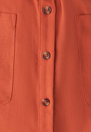 Lühikeste varrukatega oranž särk kahte plaastritaskut ja neli pruuni nööpi ees, valmistatud tekstuurses kangas.