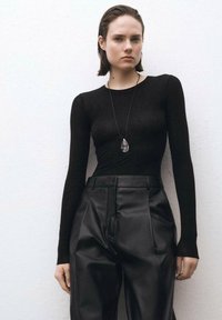 Black long-sleeve fitted top made of smooth fabric, paired with high-waisted black leather trousers featuring a pleated front.