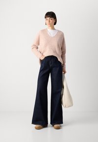 Hellrosa, strukturierter Oversized-Pullover kombiniert mit dunkelblauen, weit geschnittenen Jeans. Dazu eine cremefarbene Tasche und beigefarbene Schuhe.