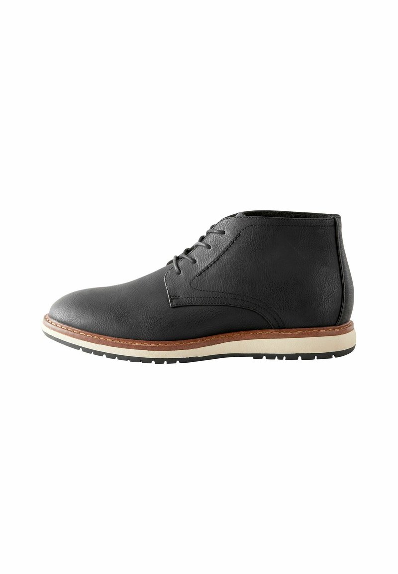 Botas de tobillo de cuero negro con una textura suave, diseño de cordones, suela de color claro y una franja marrón en contraste en la base.