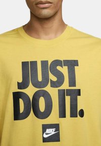 Camiseta de algodón amarilla con un atrevido estampado negro de la frase "JUST DO IT." y un pequeño logo negro de Nike en la parte inferior.