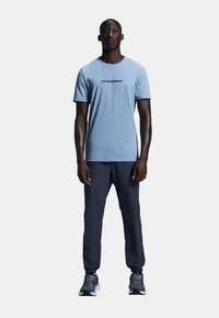 Light blue short-sleeve t-shirt with black "ON RUNNING" logo, paired with dark navy pants and gray running shoes with black accents.