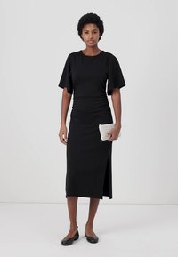 Black midi dress with short, flared sleeves, bodycon fit, side slit, and a smooth texture. Accessories include a small striped clutch and flats.