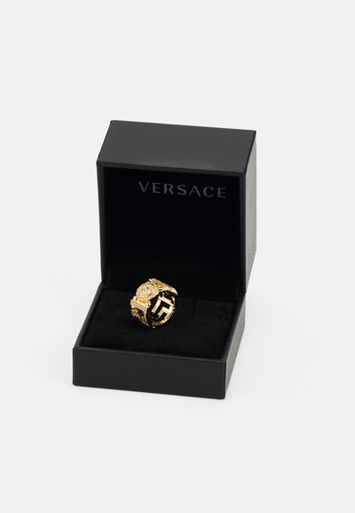 Zlatni prsten s istaknutim logotipom i složenim detaljima, predstavljen u crnoj Versace kutiji s mekim crnim oblogom.