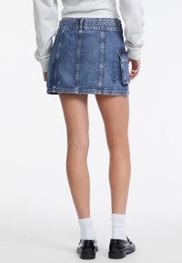 Donkerblauwe denim mini-jurk met een aansluitende taille, zichtbare stiksels en een zijzak. Zachte textuur met subtiele slijtage.