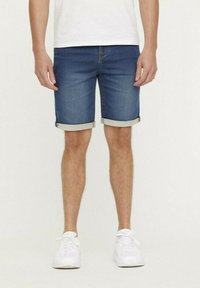 Donkerblauwe denimshorts met omgeslagen zomen, met een klassieke vijf-pocketontwerp en een lichte textuur. Gedragen met witte sneakers.