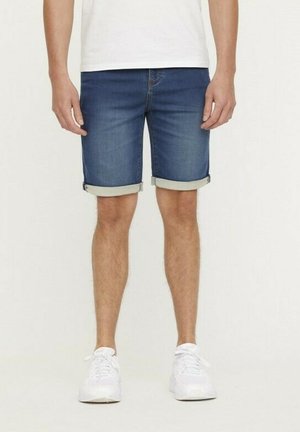 Shorts en denim bleu foncé avec ourlets retroussés, arborant un design classique à cinq poches et une texture légère. Portés avec des baskets blanches.
