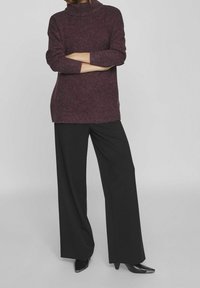 Pull à col roulé bordeaux, coupe décontractée avec ourlet côtelé ; associé à un pantalon noir ample et des chaussures noires pointues.
