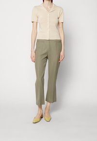 Camicetta beige a maniche corte con bottoni abbinata a pantaloni verde oliva a culotte e scarpe con tacco quadro giallo chiaro. Texture morbide, vestibilità su misura.