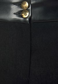 Zwarte stof met een zachte leren tailleband met twee gouden knopen. De textuur is zacht met een subtiele glans.