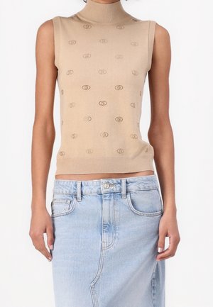 Beiger ärmelloser Rollkragenpullover mit kleinen wiederholten ovalen Mustern, kombiniert mit einem hoch taillierten hellblauen Jeansrock.