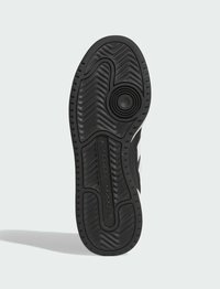 Suela de una zapatilla que presenta un material de goma negra texturizada, con un detalle circular y patrones de banda de rodadura pronunciados para mayor tracción.