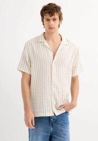 Camisa de manga corta, con cuello, en color crema con rayas verticales azules, que presenta un cierre de botones en la parte delantera y un corte relajado. Fabricada en tejido texturizado.