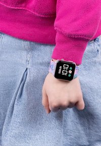 Orologio digitale con un display quadrato nero, cinturino rosa con Stitch e motivi floreali, indossato su una mano con un abbigliamento in denim.