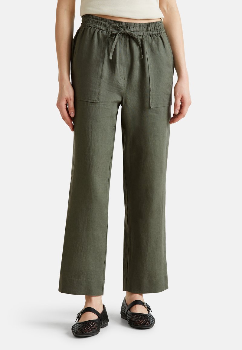 Pantalones de lino verdes con un corte relajado que presentan una cintura elástica, cordón y dos bolsillos frontales. Combinados con zapatos negros perforados.