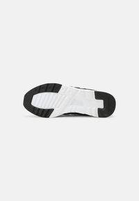 Semelle d'une basket avec un motif de bande de roulement en caoutchouc noir et blanc présenté sur un fond clair uni.