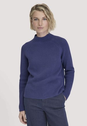 Gebreide trui in donkerpaars, met een hoge kraag, geribbelde textuur en nauwsluitende mouwen. Gecombineerd met donkerblauwe broek.