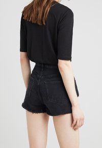 Top negro de mangas cortas combinado con pantalones cortos de mezclilla negros de talle alto, con dobladillos deshilachados y detalles desgastados, visto desde la parte posterior.