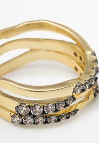 Anello multibanda in oro con design ondulato, caratterizzato da piccoli cristalli chiari rotondi incastonati in accenti neri lungo una banda.