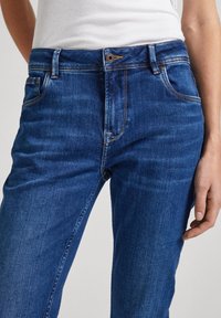 Modré džíny z denimu s klasickým designem, středně vysokým pasem, pěti kapsami a kontrastními švy. Hladká textura látky.