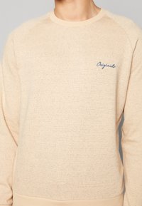 Sweatshirt beige con motivo a maglia testurizzata, collo a giro e ricamo blu "Originals" sul petto. Presenta maniche raglan.