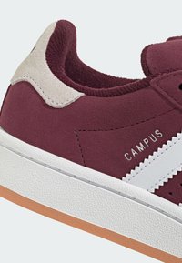 Donkerrode suède sneaker met beige hielkap, witte zigzagzijstreep, "CAMPUS" branding en een gestructureerde witte zool met een gumkleurige buitenzool.