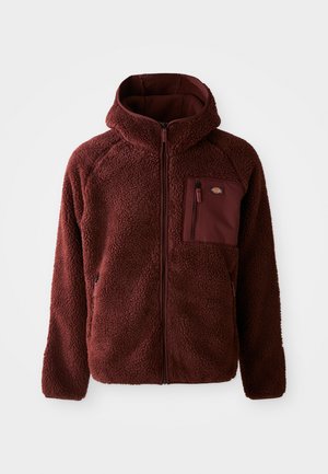 Burgundy fleece jacket with a zip front, hood, side pockets, and chest pocket. Textured, soft material with a slightly oversized fit.