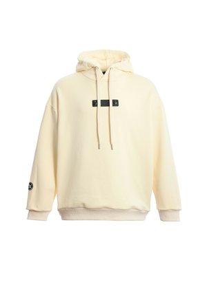 Sudadera crema con capucha ajustable, parche negro en la parte frontal y puños sutiles. Textura suave y corte relajado, con un logo en la manga.
