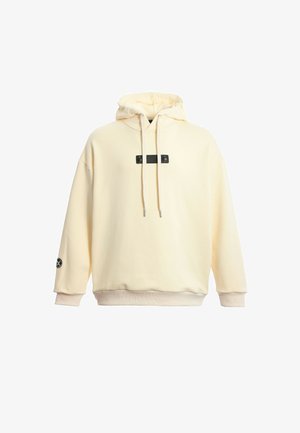 Sudadera crema con capucha ajustable, parche negro en la parte frontal y puños sutiles. Textura suave y corte relajado, con un logo en la manga.