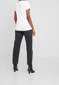 Camiseta blanca de manga corta combinada con jeans gris oscuro, de corte recto y con dobladillo deshilachado. Botines negros de tacón completan el look.