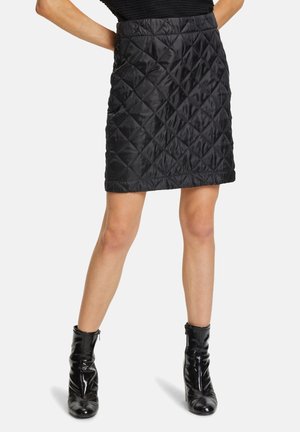Falda acolchada negra con un patrón de diamantes, diseño hasta la rodilla, con una textura suave y cinturilla elástica. Combinada con botines negros brillantes.