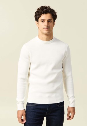 Maglione bianco a maniche lunghe, con scollatura a girocollo e texture, abbinato a jeans scuri. Il tessuto presenta un delicato motivo a costine.