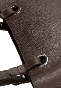 Borsa a tracolla in pelle marrone con una superficie testurizzata, dettagli in metallo argentato e un logo del marchio visibile. Presenta una tracolla rinforzata e un dettaglio ad anello.