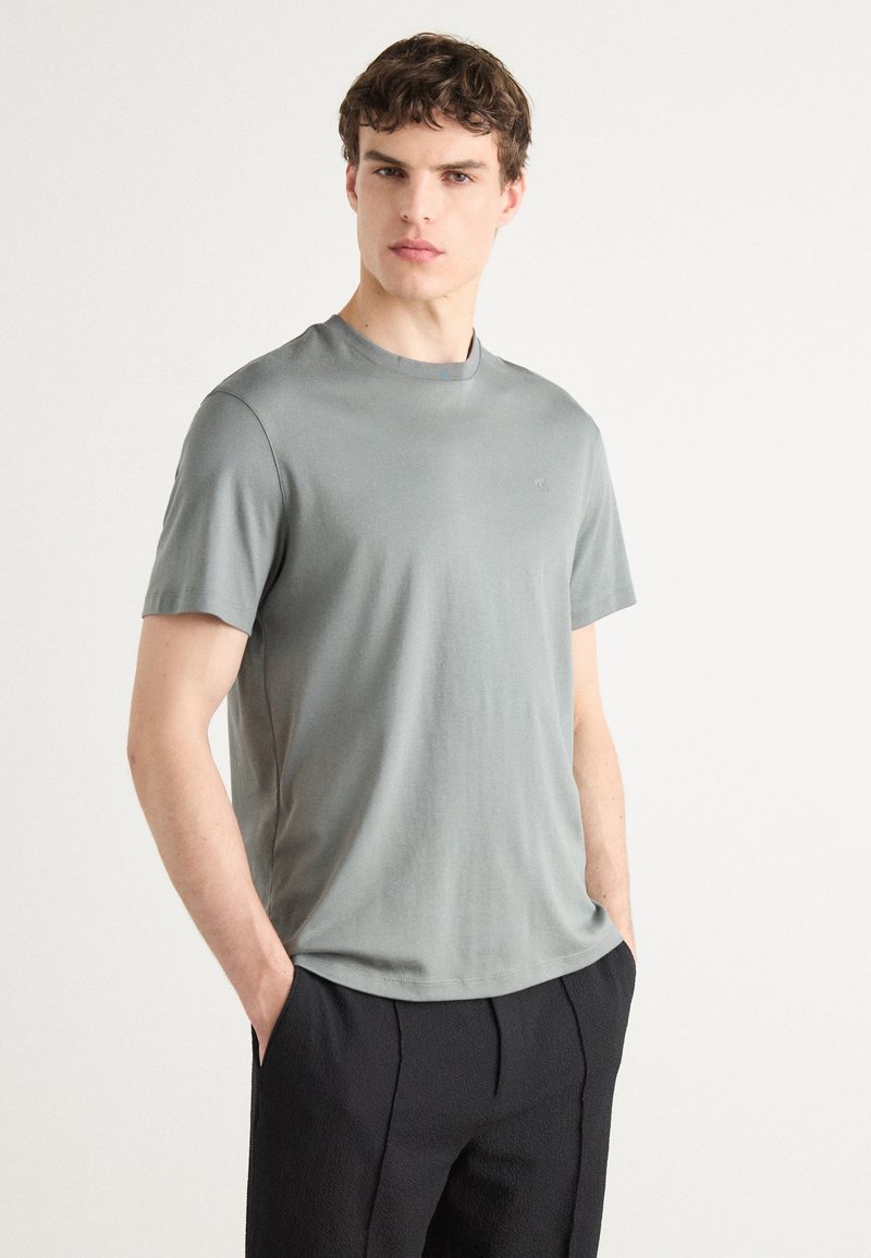 Tricou gri cu mânecă scurtă și decolteu rotund, fabricat dintr-un material neted. Are un logo minimalist pe partea stângă a pieptului. Croială lejeră.