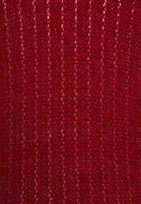 Tejido de punto acanalado rojo con textura suave y brillo ligero, que presenta líneas verticales y un tejido con patrón a lo largo de toda la tela.